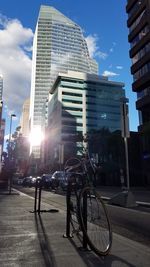 Bicycle by modern buildings in city against sky