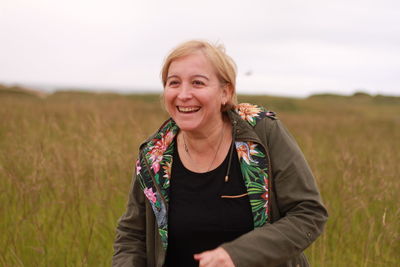 Portrait of smiling woman standing on field against sky