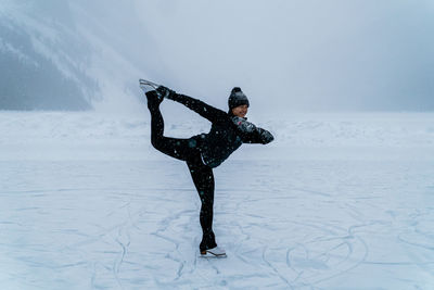 Female ice skater skating on frozen lake outside in snowstorm near forest in canada.
