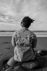 Rear view of woman sitting on rock at beach