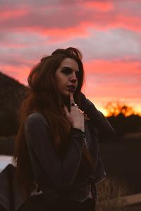 Beautiful young woman standing against sky during sunset