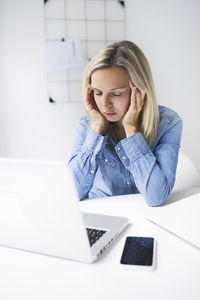 Stressed businesswoman with head in hand sitting at office