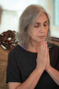 Senior woman with eyes closed praying at home