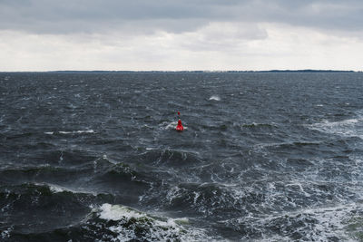 Scenic view of rough sea with navigation buoy against sky