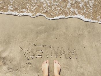 Low section of woman standing with text on wet sand at beach