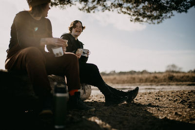 Low angle view of smiling mother and daughter holding cup sitting in forest