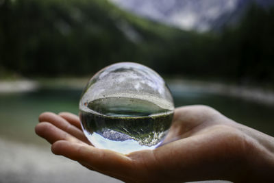 Cropped hand holding crystal ball against lake