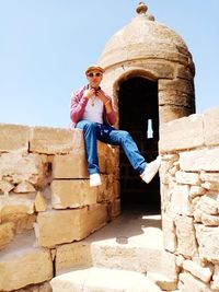 Portrait of man sitting on built structure against clear sky