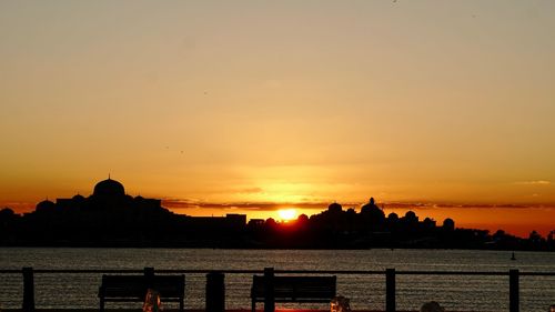 Silhouette buildings by sea against sky during sunset