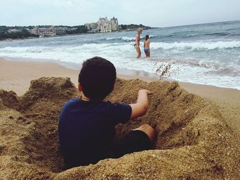 Boy sitting amidst sand at beach