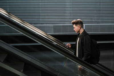 Young man using smart phone on escalator