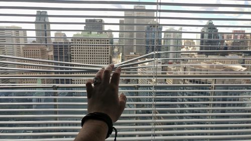 Close-up of hand holding curtains against sky in city