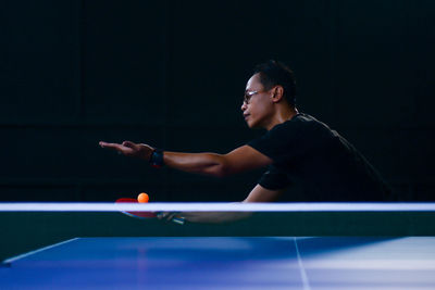 Young man playing table tennis in dark