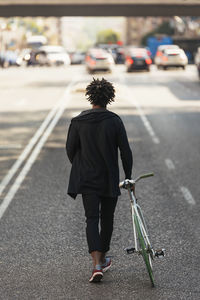 Rear view of man walking with bicycle on road