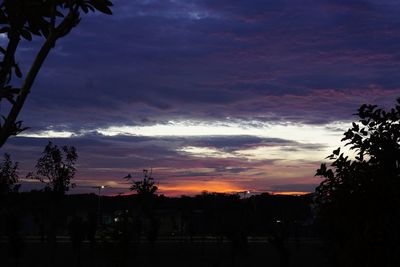 Silhouette trees against dramatic sky at sunset