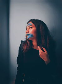 Young woman with face paint looking away while standing against wall