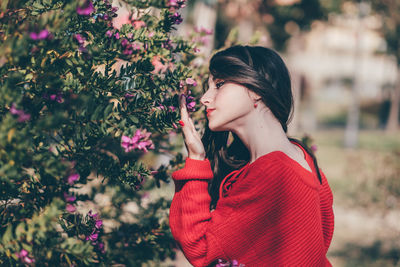 Side view of woman standing by red flowering plants