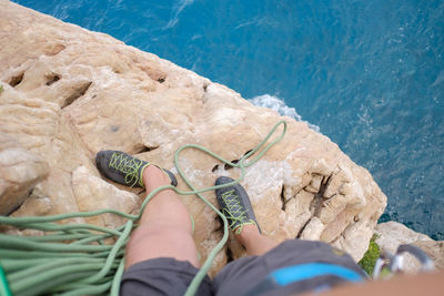 Low section of man with rope standing on rock by sea