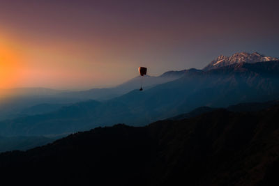 Paragliding in mountains against sky during sunset