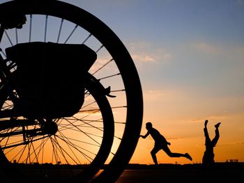 Silhouette people by bicycle against sky during sunset