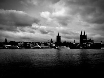 View of buildings by river against cloudy sky