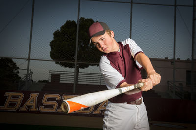 Portrait of a high school baseball player in maroon uniform swing his bat