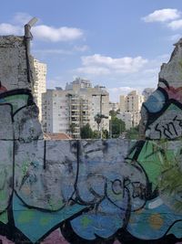 Graffiti on wall by buildings in city against sky