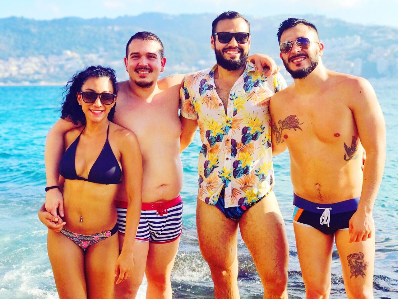 happiness, leisure activity, vacations, sunglasses, young adult, real people, lifestyles, smiling, standing, summer, young men, bikini, shirtless, sea, front view, outdoors, togetherness, looking at camera, portrait, sunlight, fun, young women, sky, water, day, nature, beach, cheerful, friendship, beauty in nature