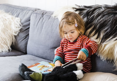 Baby girl reading picture book while sitting on sofa at home