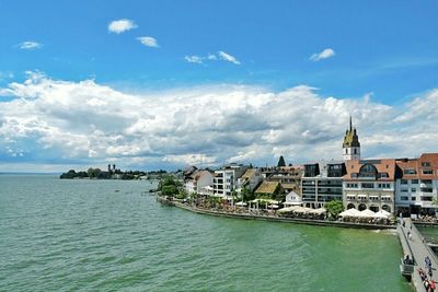 Buildings by sea against cloudy sky