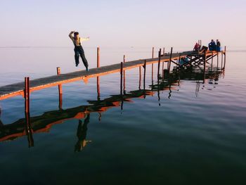 People standing on sea against clear sky during sunset