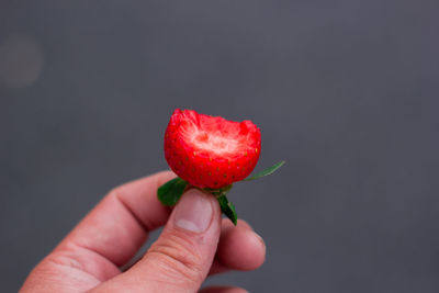 Close-up of hand holding eaten strawberry against gray background