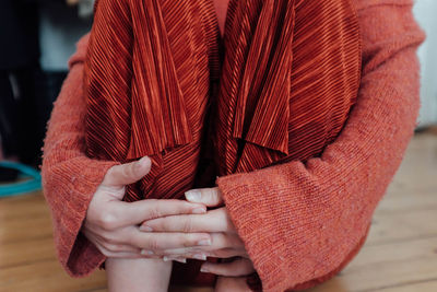 Midsection of woman hugging knees on hardwood floor