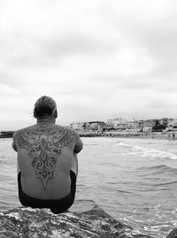 Rear view of man standing on rock at beach against sky