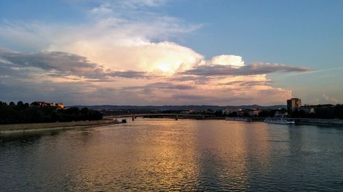 City by river against sky during sunset