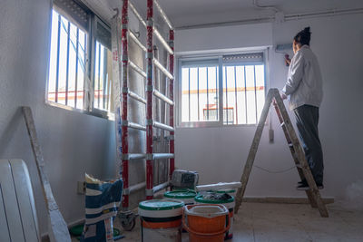 Young woman painting interior wall with white paint. paint cans and painter ladder.
