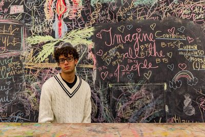 Portrait of teenage boy standing against blackboard