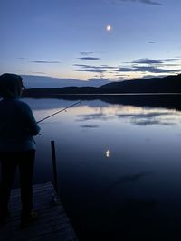 Rear view of man standing by lake against sky