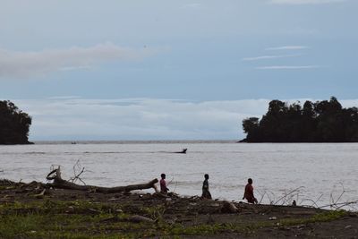 People sitting on beach by sea against sky