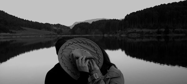 Couple romancing behind hat against lake and mountains