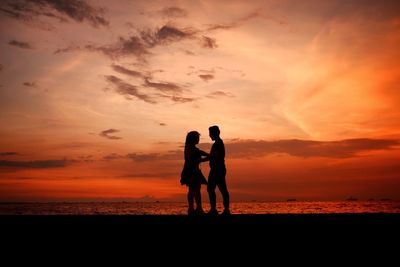 Silhouette friends standing on beach against sky during sunset