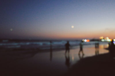 Silhouette people walking on beach against sky during sunset