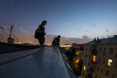 Man and woman on building terrace against sky at dusk