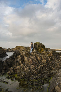 Woman standing on rock by sea against sky