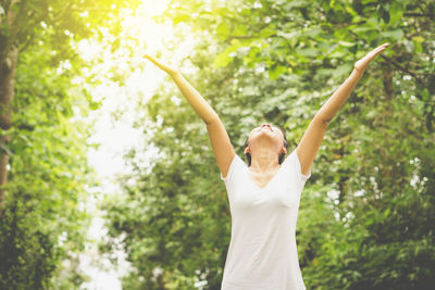 Woman with arms raised standing against trees