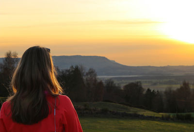 Rear view of woman standing on field against sky during sunset