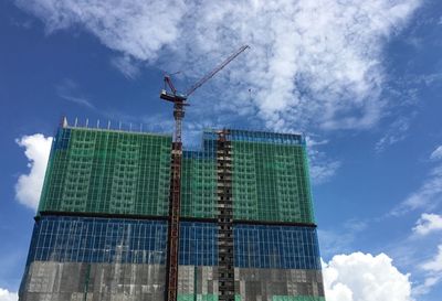 Low angle view of crane by building against sky