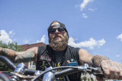 Portrait of man riding motorcycle on sunglasses against sky