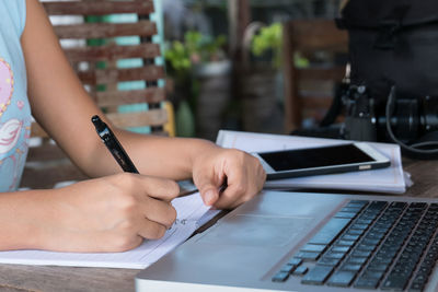 Woman writing on book by laptop and smart phone at table
