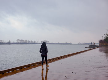 Rear view of woman standing on pier over sea against sky